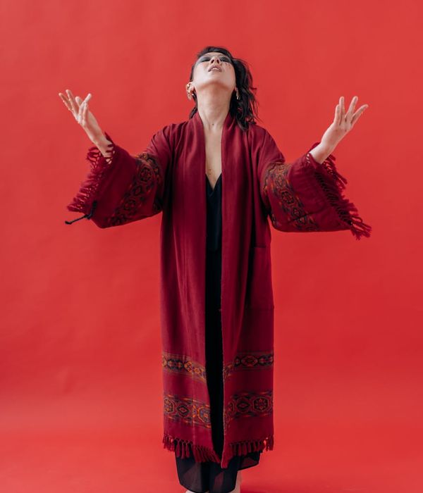 A woman in a calm, focused yoga pose against a lilac background.